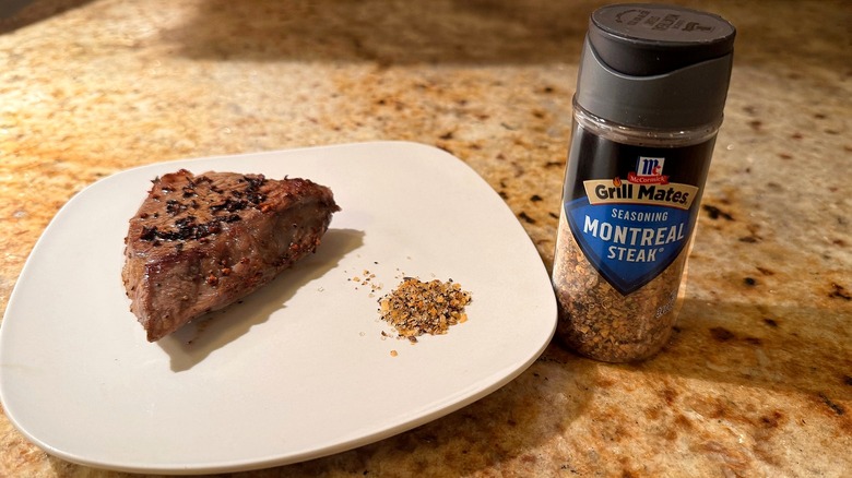 container of seasoning next to plate with steak