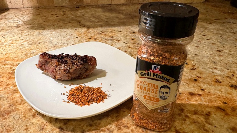 container of seasoning next to plate with steak