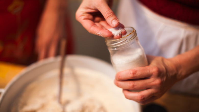 A home baker adds flaky salt to her pizza dough bowl