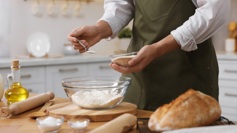 A home baker adds dry yeast to his pizza dough