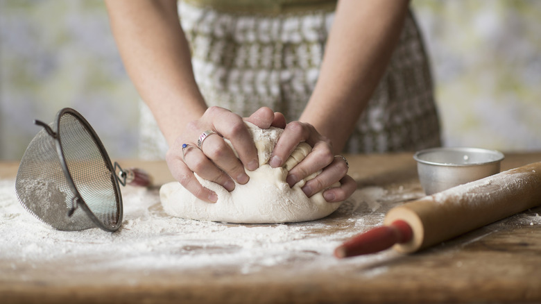 A baker kneads dough with a roller on a floured surface