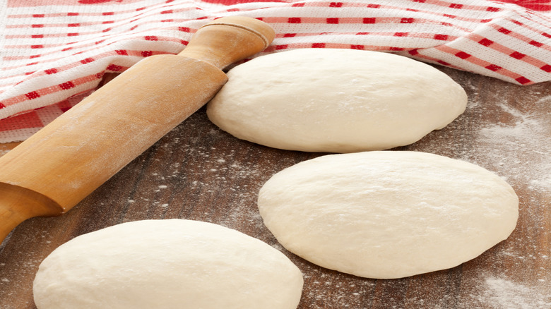 A small pizza dough ball is next to a roller and towel on the counter