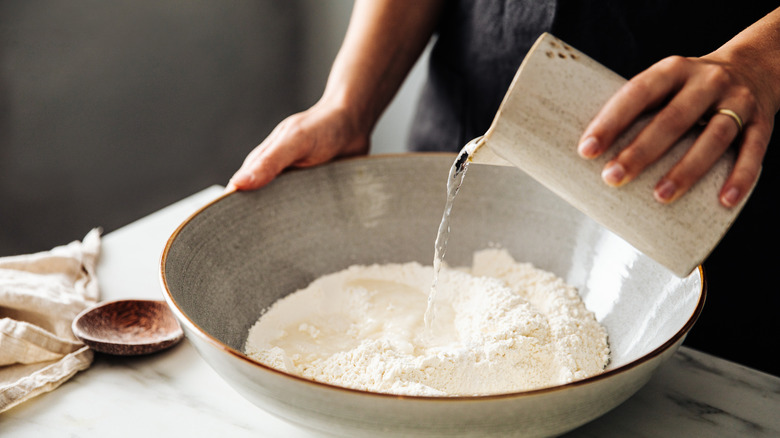 A baker adds water to her flour mixture to make pizza dough