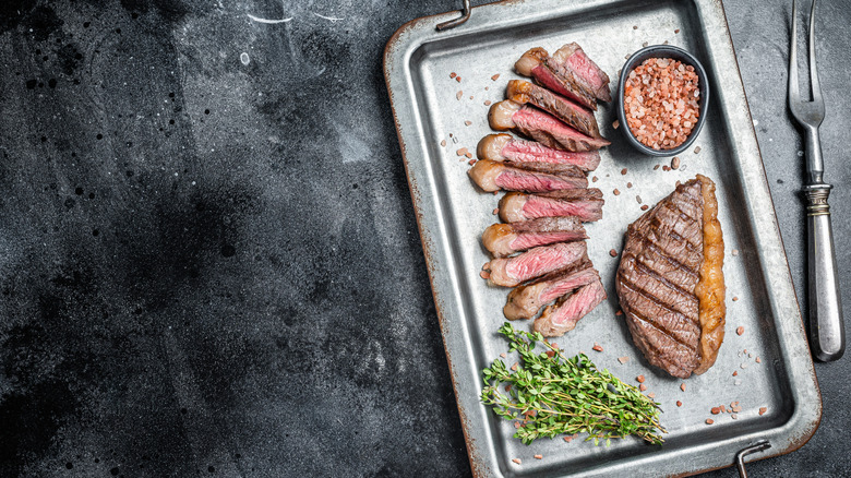Grilled and sliced top sirloin on baking sheet, with peppercorns and fresh thyme