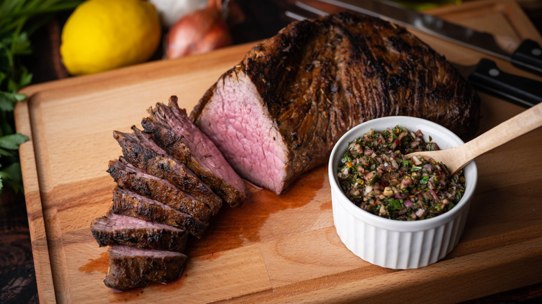Sliced, grilled tri-tip steak with chimichurri sauce, on a cutting board
