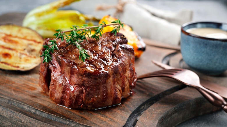 Thick-cut grilled filet mignon, garnished with thyme, on a cutting board
