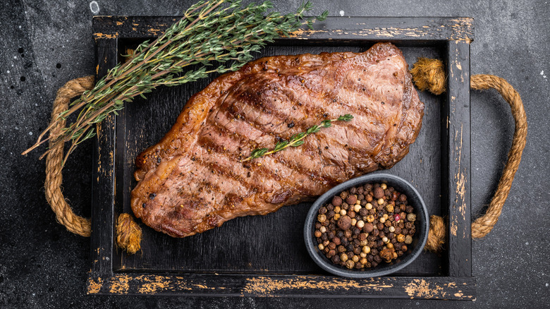 Barbecued New York strip on black rectangular platter with fresh thyme and peppercorns