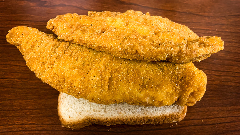 two pieces of fried catfish on top of a slice of white bread
