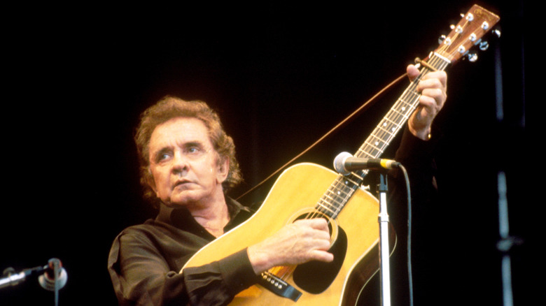 Johnny Cash raising his acoustic guitar while performing