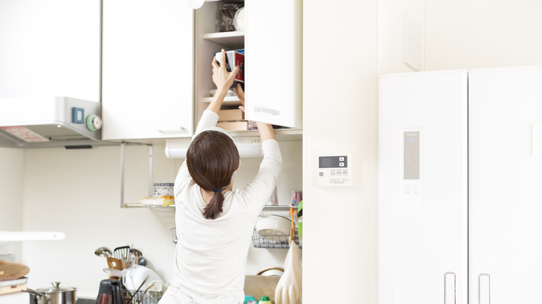 woman reaches up to high kitchen cabinet
