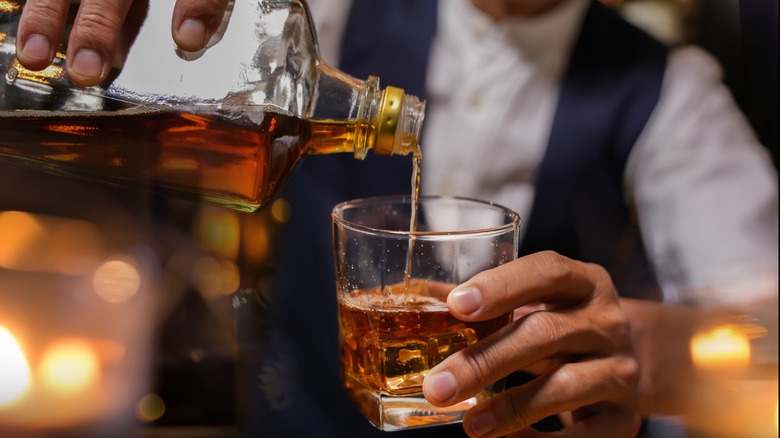 A bartender pouring bourbon into a rocks glass.