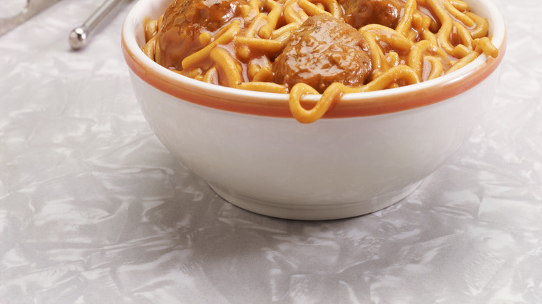 Spaghetti and meatballs in a bowl on a white table with a can opener and can