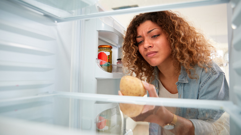 A woman looking at a sprouted potato in the fridge