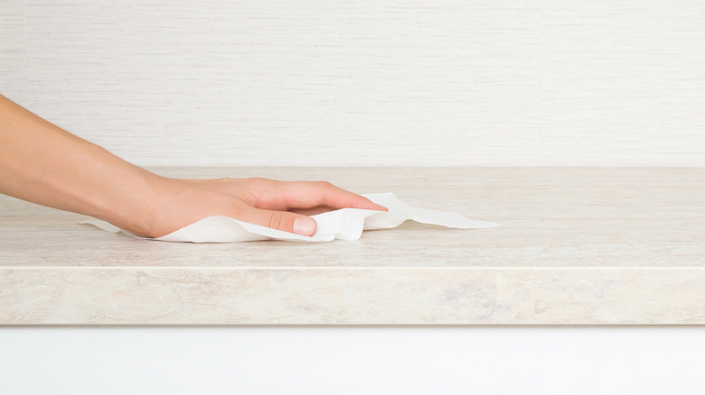 Person wiping a counter with a disinfectant wipe or paper towels