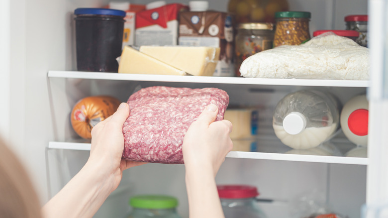 Person taking a package of ground meat out of a fridge.
