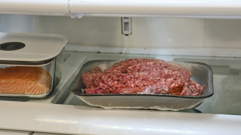 Ground beef stores on fridge shelf next to a container of fish