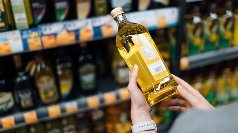 Close up on a person shopping in an oil section of a grocery store, holding a bottle to look at the label.