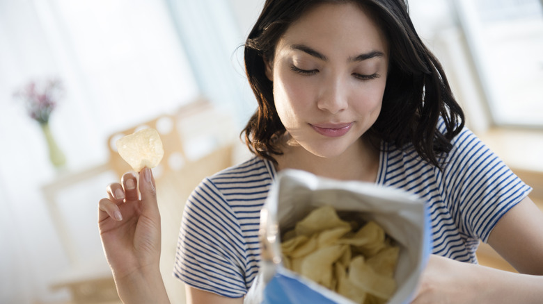 A woman holding a potato chip and a bag of potato chips