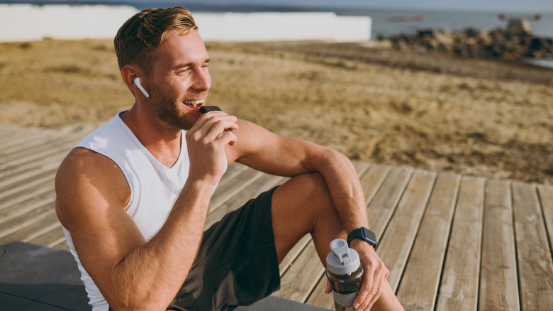 A man outdoors eating a protein bar and holding a water bottle