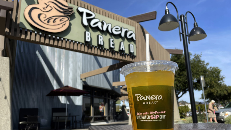 Panera charged lemonade in a takeout cup, in front of a restaurant storefront