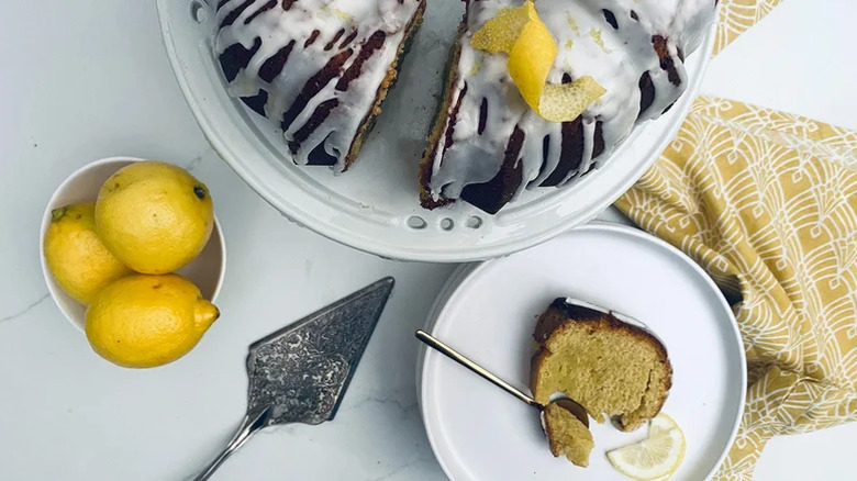 Slice of lemon olive oil bundt cake, cut from a cake with white frosting and a lemon zest garnish
