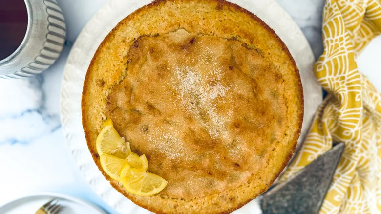 A whole, freshly baked lemon olive oil dump cake, topped with lemon wedges and a little confectioners' sugar