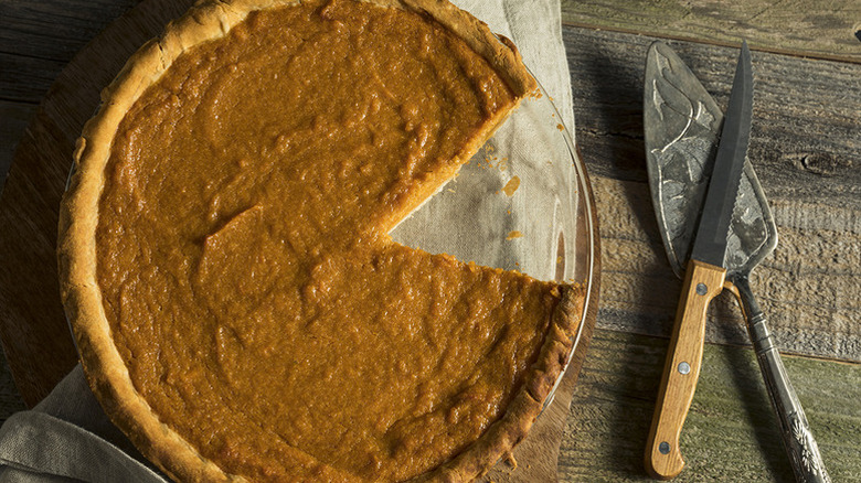 A sweet potato pie on a glass serving plate, with a wedge cut out of it