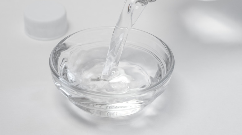 Pouring white distilled vinegar in small glass bowl