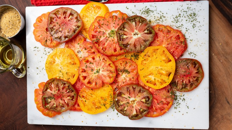 Sliced heirloom tomatoes on a white cutting board with olive oil and seasonings