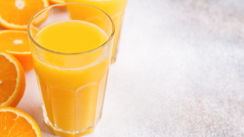 Glass of orange juice surrounded by halved oranges
