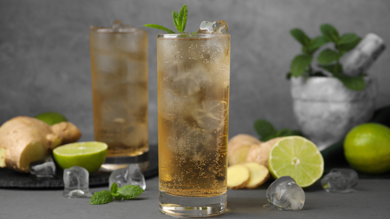 Glass of ginger ale, with limes, ginger, and ice cubes surrounding it