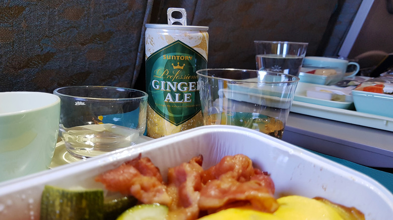 Ginger ale can and glass on airplane tray table, with an airline meal in the foreground
