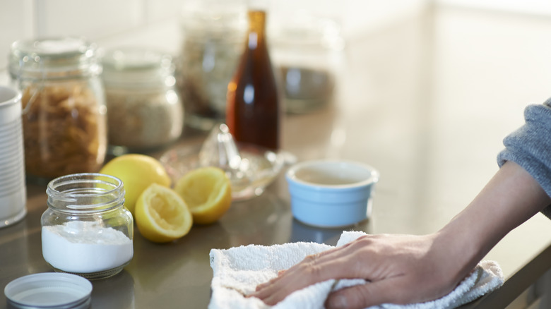 A person cleaning with lemon juice and baking soda, and wiping a kitchen counter with a towel.