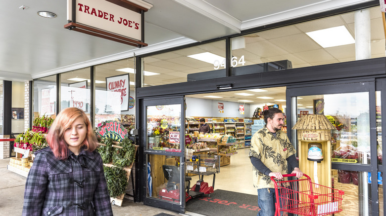 Two people exiting a Trader Joe's storefront through the glass sliding doors.