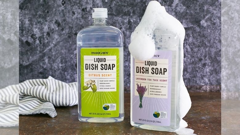 Two bottles of Trader Joe's dish soap with suds, and a striped towel in the background