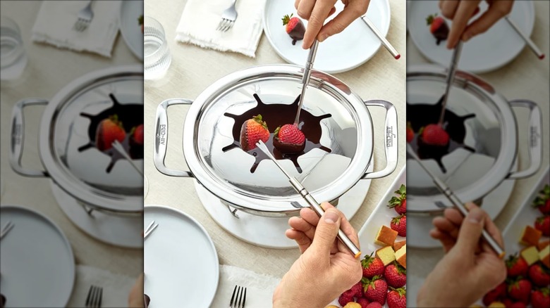 Two hands dipping strawberries into chocolate fondue