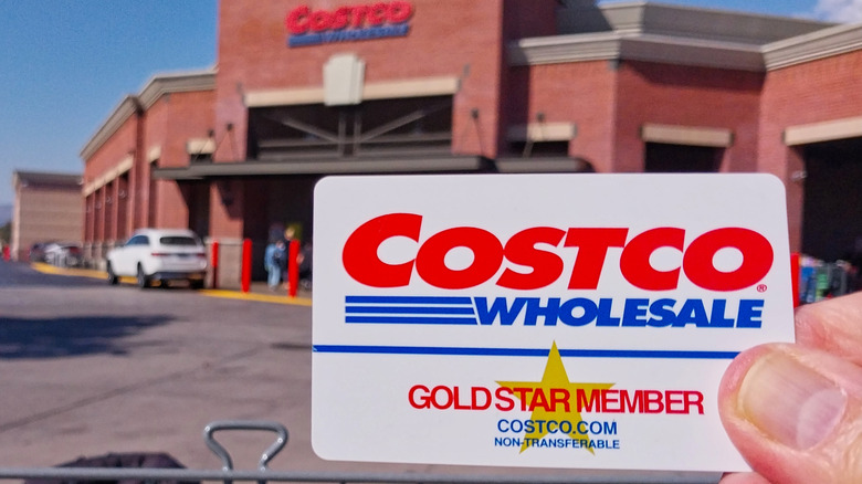 Hand holding a Costco membership card outside a Costco store