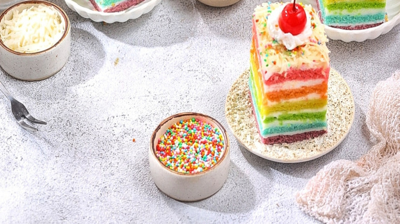 Three mini plates with slices of rainbow cake, each garnished with a bright red cherry.