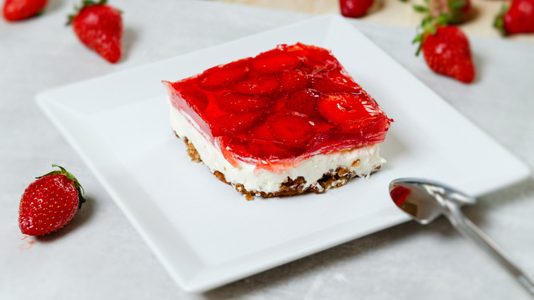 A square of strawberry pretzel tart on a white plate with fresh strawberries adorning the table.