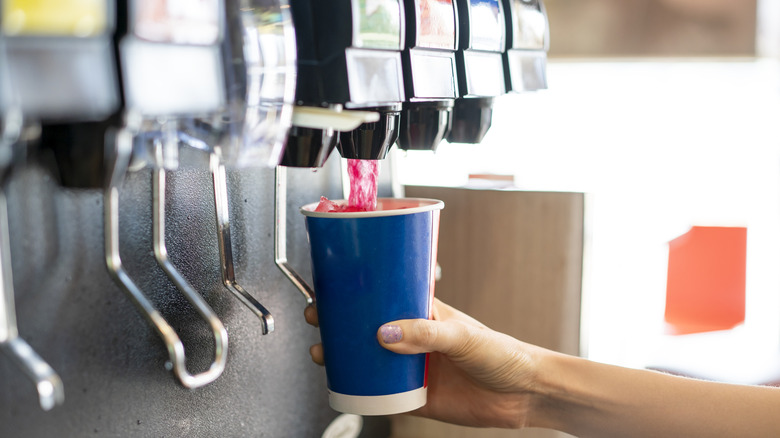 close-up of a person pouring soda into a cup from a soda fountain