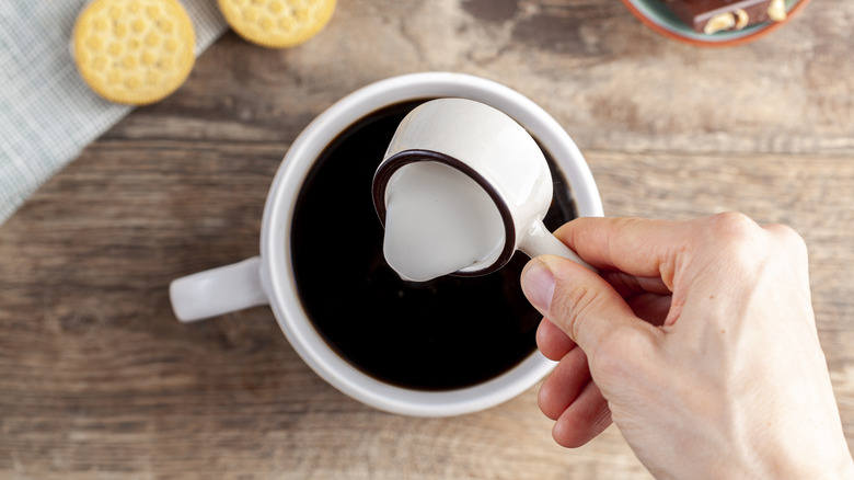 person adding creamer to coffee