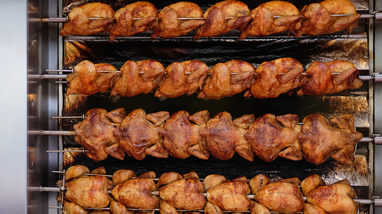 Rows of rotisserie chickens cooking on spits