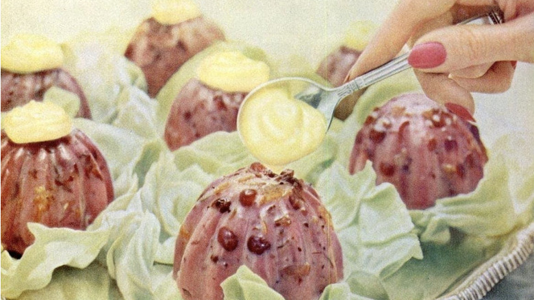 A vintage ad of a woman topping a cranberry souffle salad with a dollop of mayonnaise