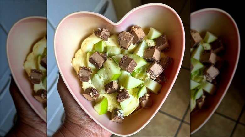 A person holding a heart shaped bowl of Snickers salad with apples