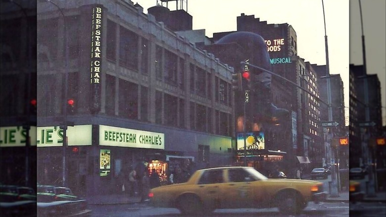 Old image of a Beefsteak Charlie's, on the corner of a busy street, as a yellow cab speeds past