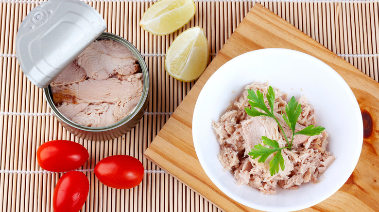 Opened can of tuna fish alongside bowl of flaked tuna from a can