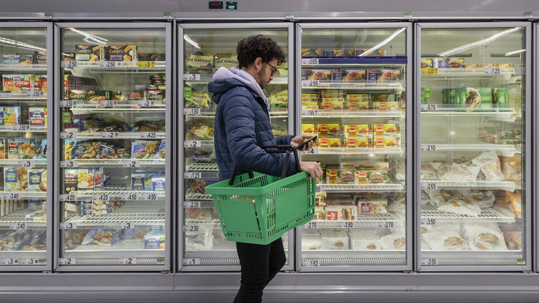 Shopper on phone while passing through a grocery store's frozen food aisle