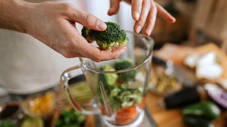 person putting broccoli in blender 