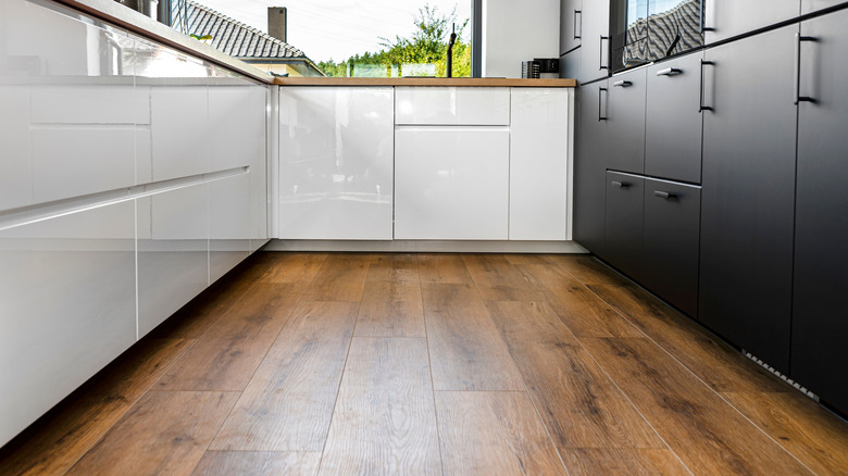 Vinyl floor in galley kitchen is lined on three sides with modern white and black cabinetry