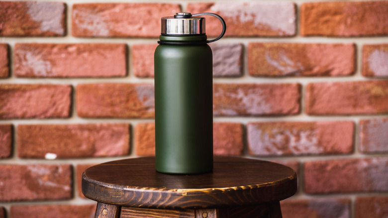 Dark green thermos before brick wall